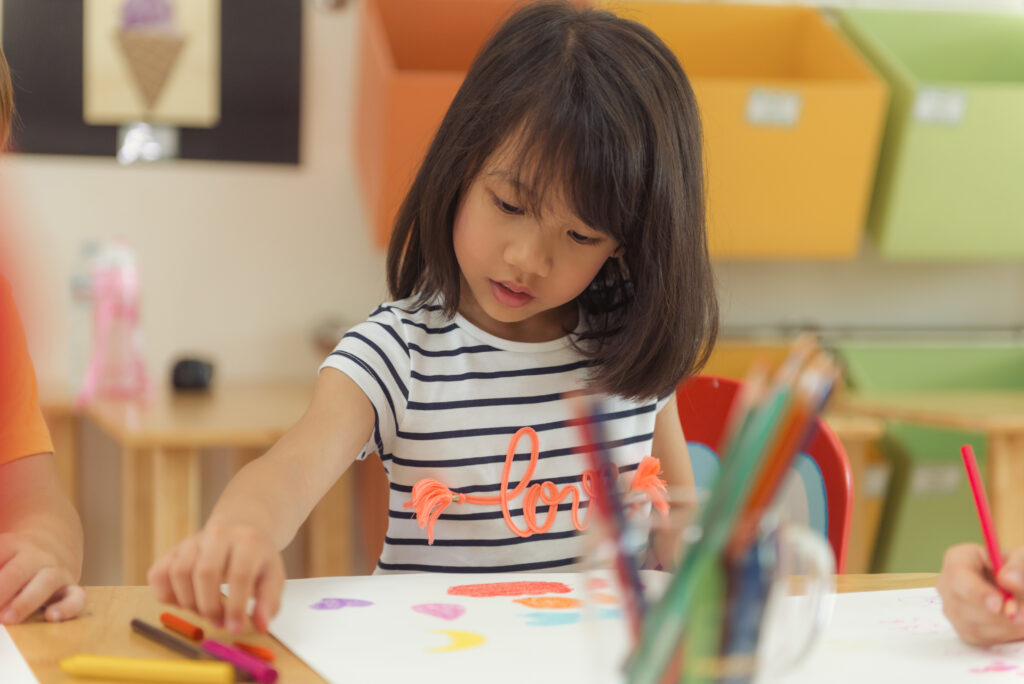 Girl drawing color pencils in kindergarten classroom, preschool